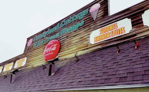 Sign for "Candyland Cottage & Ice Cream Shoppe" featuring ice cream cones, Coca-Cola logo, and menu items like sundaes.
