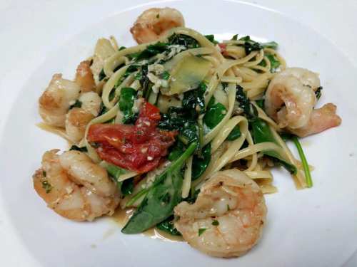A plate of linguine pasta topped with shrimp, spinach, and sun-dried tomatoes in a creamy sauce.