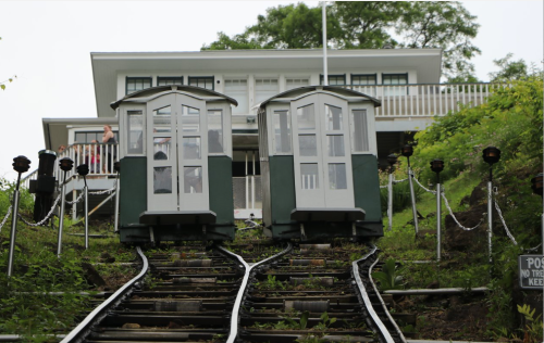 Two vintage cable cars on tracks leading up to a white building with a porch, surrounded by greenery.