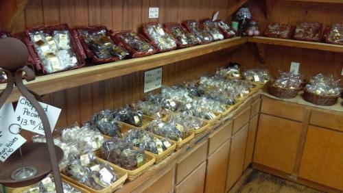 A wooden shelf filled with various packaged sweets and treats, including chocolates and candies, in a cozy shop.