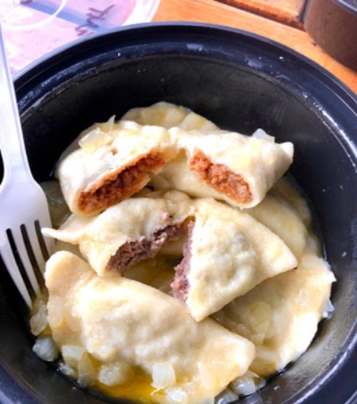 A black bowl filled with dumplings, some cut open to reveal a meat filling, surrounded by chopped onions and sauce.