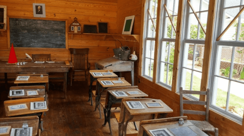 A vintage classroom with wooden desks, a chalkboard, and large windows, creating a warm, inviting atmosphere.