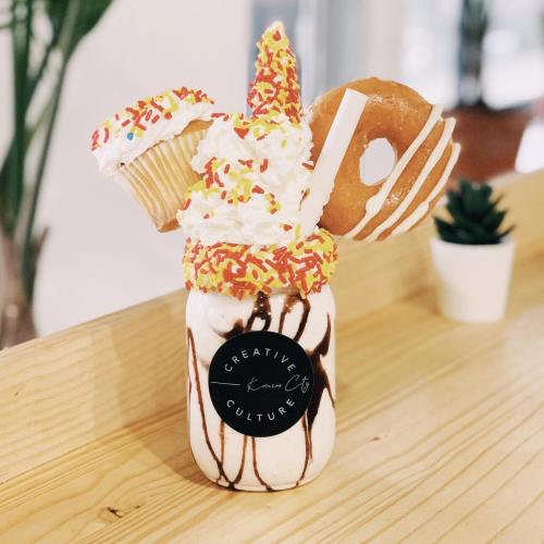 A decadent milkshake topped with whipped cream, a cupcake, a donut, and colorful sprinkles in a jar.