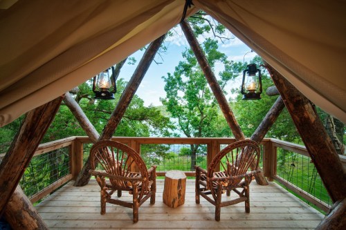 Cozy wooden deck with two chairs and lanterns, surrounded by trees and a scenic view.