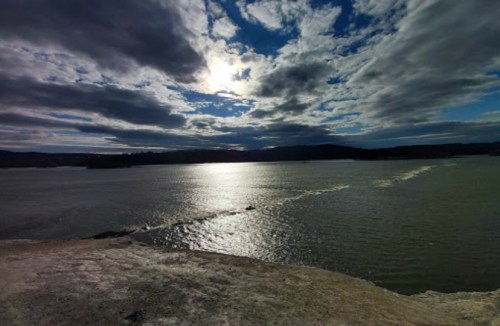 A serene view of a river under a cloudy sky, with sunlight reflecting on the water's surface.