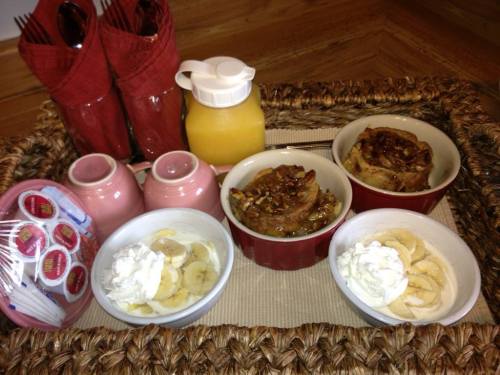 A tray with two bowls of dessert topped with bananas and whipped cream, alongside orange juice and napkins.