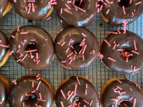 A close-up of chocolate-glazed donuts topped with pink sprinkles on a cooling rack.