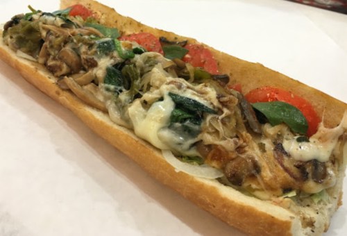 A loaded sandwich with melted cheese, mushrooms, spinach, tomatoes, and lettuce on a toasted sub roll.