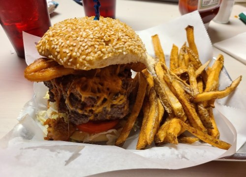 A sesame seed burger topped with cheese and onion rings, served with a side of crispy French fries.