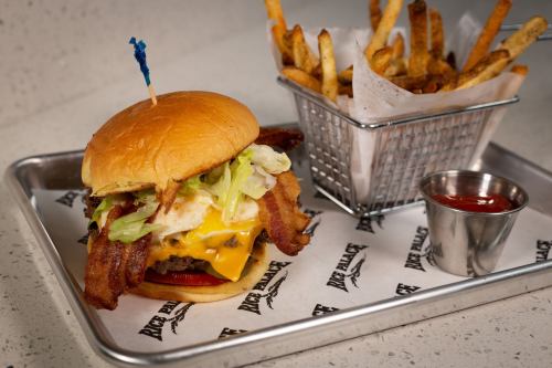 A juicy burger with bacon, cheese, lettuce, and a fried egg, served with a side of fries and ketchup on a tray.