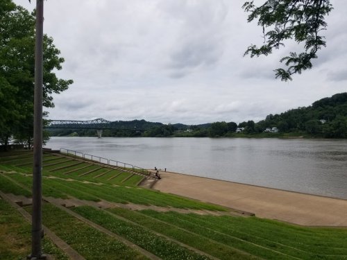 A calm river scene with grassy steps, a bridge in the distance, and overcast skies.