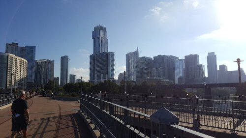 A scenic view of a city skyline with tall buildings under a clear blue sky, seen from a walkway.