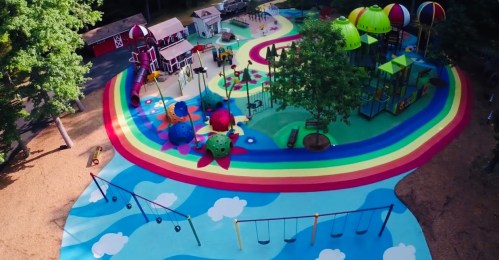 Aerial view of a colorful playground with slides, climbing structures, and swings surrounded by vibrant rainbow patterns.