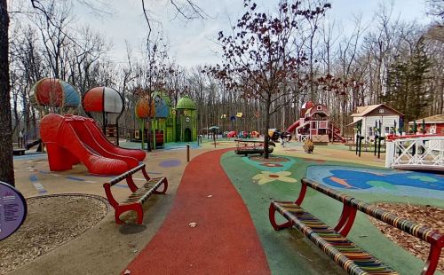 Colorful playground with unique structures, including large slides and playhouses, surrounded by trees in a wooded area.
