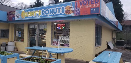 Exterior of Sunny's Donuts shop, featuring a colorful sign and outdoor seating, with a "Voted Best Donut Shop" banner.