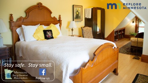 Cozy bedroom with a wooden bed, yellow walls, and decorative pillows, promoting Minnesota Bed & Breakfast Association.