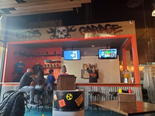 Interior of a casual bar with a skull-themed sign, TVs showing sports, and patrons seated at the counter.