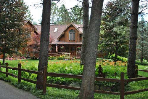 A charming wooden house surrounded by trees and colorful flowers, with a wooden fence in front.