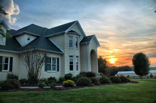 A beautiful house with a landscaped yard at sunset, featuring vibrant flowers and a scenic sky.