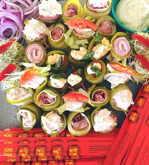 A colorful platter of rolled pickles filled with meats, vegetables, and sauces, surrounded by chopsticks and garnishes.