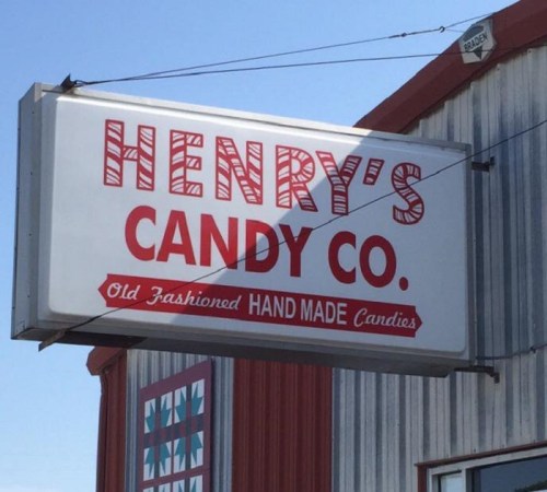 Sign for Henry's Candy Co. featuring "Old Fashioned Hand Made Candies" in bold red letters against a metal background.