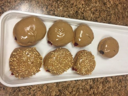 A tray of six donuts, three topped with chocolate icing and three with nuts and cherry filling.