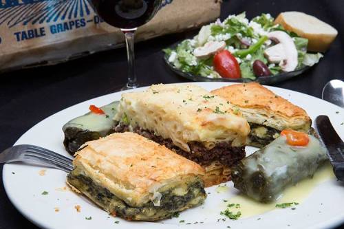 A plate of assorted pastries, including spinach and meat-filled dishes, served with a side salad and a glass of red wine.