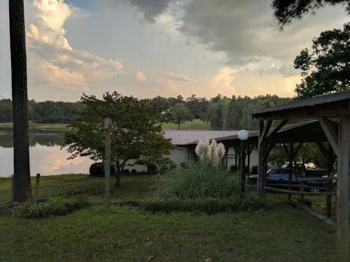 A serene lakeside view with a house, trees, and a gazebo under a cloudy sky.