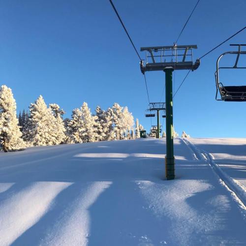 Ski lift against a clear blue sky, surrounded by snow-covered trees and a pristine white landscape.
