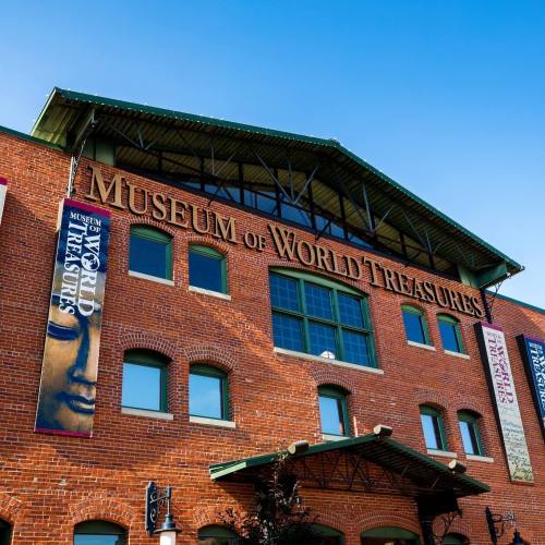 Exterior of the Museum of World Treasures, featuring brick walls and large windows under a clear blue sky.