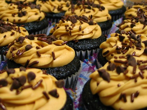 A close-up of chocolate cupcakes topped with creamy peanut butter frosting and chocolate sprinkles.