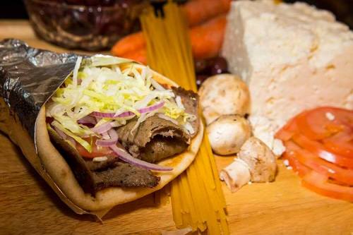 A close-up of a wrapped sandwich filled with meat, lettuce, and tomatoes, surrounded by vegetables and cheese.