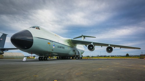 A large military aircraft on a tarmac under a cloudy sky, showcasing its distinctive design and wingspan.