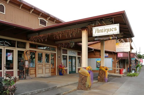 A storefront labeled "Antiques" with festive lights, surrounded by shops and decorations in a quaint setting.