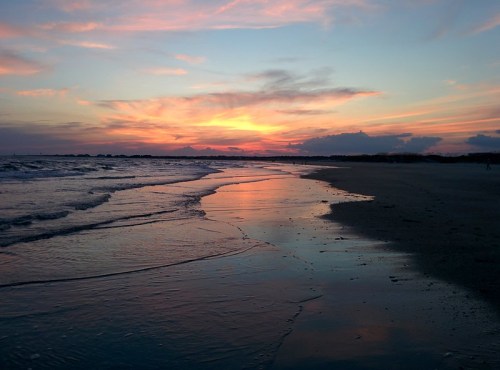 A serene beach at sunset, with colorful skies reflecting on the water and gentle waves lapping at the shore.