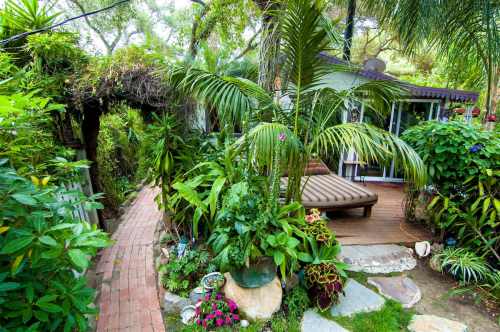 Lush garden path leading to a cozy deck surrounded by tropical plants and vibrant flowers.