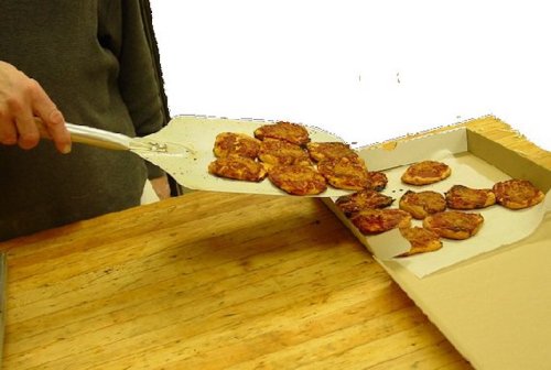 A person using a spatula to lift cooked patties from a tray onto a wooden table.