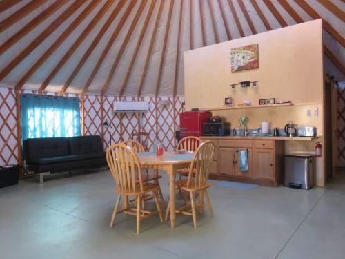 Interior of a yurt featuring a dining table, chairs, kitchenette, and a cozy seating area with a futon.