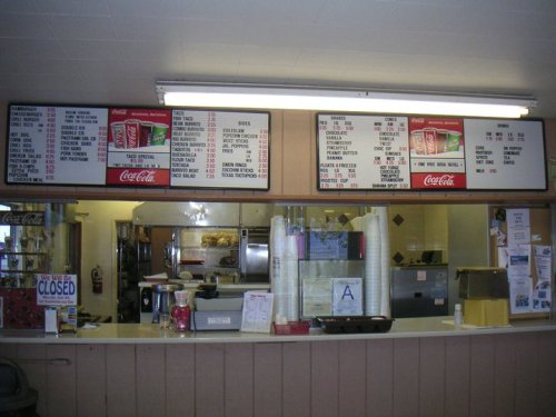 Menu board displaying food and drink options at a diner, with prices listed above a service counter.