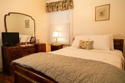 Cozy bedroom featuring a bed, dresser, mirror, lamp, and floral curtains. Warm, inviting atmosphere.