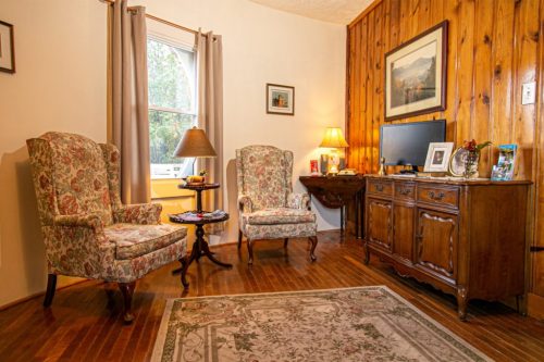 Cozy living room with floral armchairs, a wooden table, a TV, and a decorative rug on hardwood floors.
