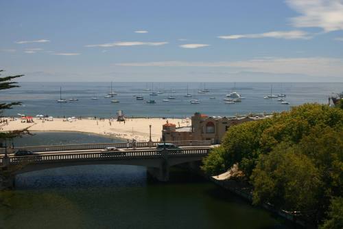A scenic view of a beach with boats in the water, a bridge crossing a river, and lush greenery along the shore.