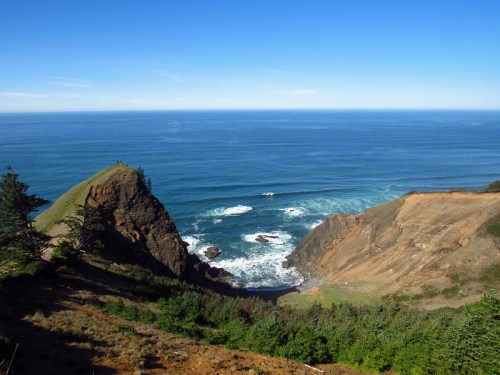 A scenic coastal view featuring cliffs, waves, and a clear blue sky over the ocean.