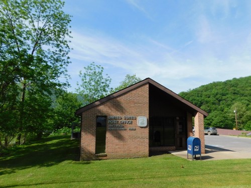 A brick building with a sign reading "United States Post Office" surrounded by greenery and a blue mailbox outside.