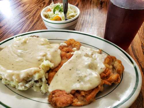 A plate of fried chicken with gravy over mashed potatoes, accompanied by a small salad and a glass of iced tea.