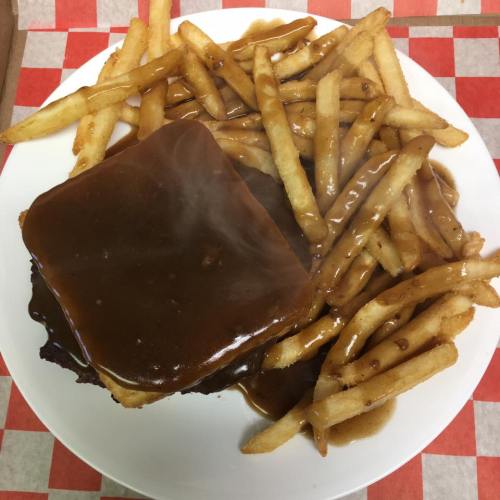 A plate of fries with a sandwich covered in brown gravy, served on a red and white checkered tablecloth.