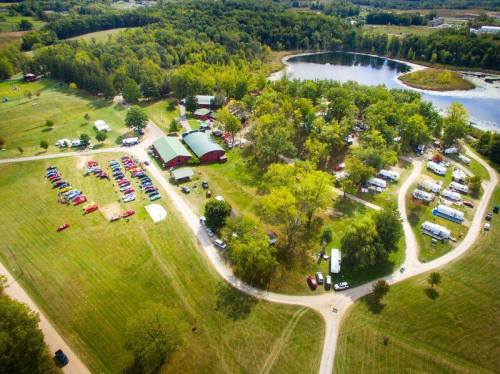 Aerial view of a park with a pond, green trees, and various tents and vehicles set up for an event.