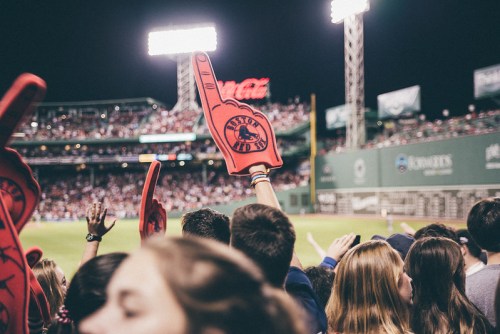 A crowd at a baseball game holds up foam fingers, cheering in a lively stadium atmosphere.