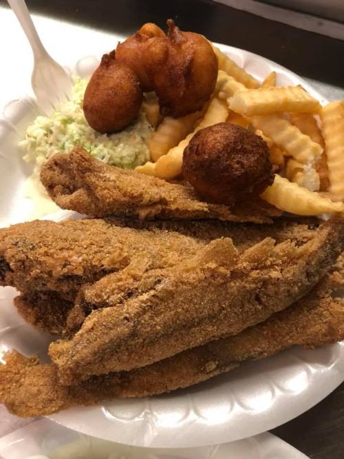 A plate of fried fish fillets, crinkle-cut fries, coleslaw, and hushpuppies.