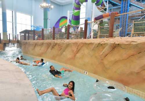 A vibrant indoor water park with a lazy river, water slides, and people floating on tubes.